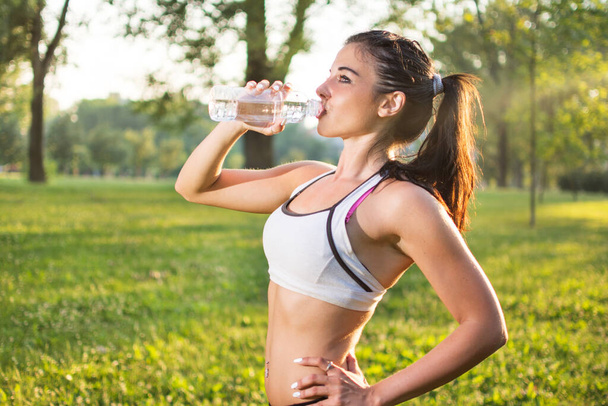 Jeune fille sportive boire de l'eau après avoir couru dans le parc au coucher du soleil - Photo, image