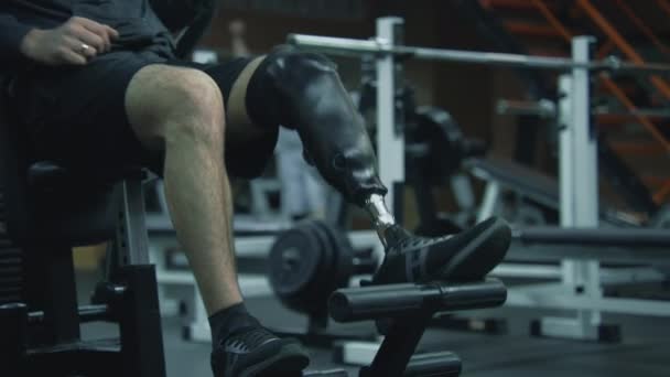 Atleta motivato con protesi sugli allenamenti delle gambe su attrezzo da allenamento nel moderno centro fitness. L'uomo sportivo adulto con disabilità fisica fa allenamento di forza utilizzando attrezzature da palestra sportive professionali. - Filmati, video
