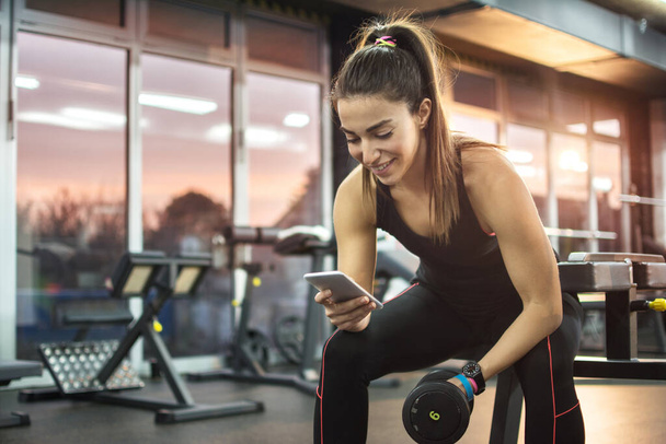 junge Frau benutzt Handy im Fitnessstudio - Foto, Bild