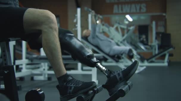 Motivated sportsman with prosthetic leg exercises on workout machine in modern gym. Athletic Caucasian man with physical disability does strength training for arms using professional sports equipment. - Footage, Video