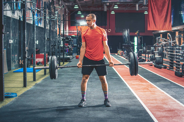 Fit Sportler in Sportbekleidung Trainingsbizeps mit schwerer Langhantel in einem modernen Fitnessstudio - Foto, Bild