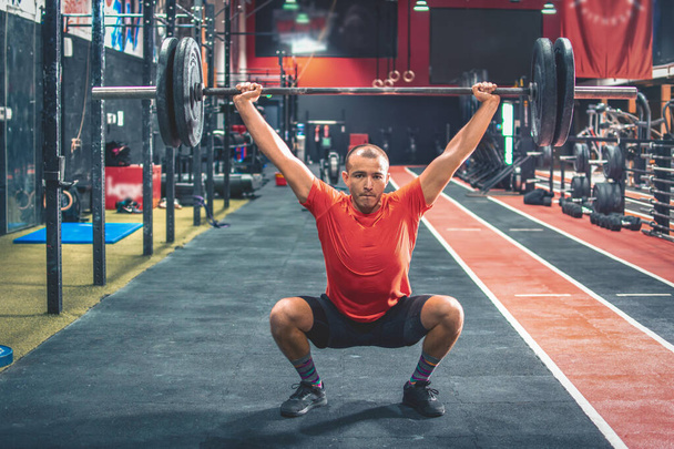 Jeune sportif masculin en forme faisant squats avec un haltère sur les épaules dans une salle de gym - Photo, image