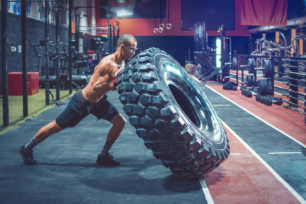 Мужчина без рубашки качает тяжелую шину в спортзале
 - Фото, изображение