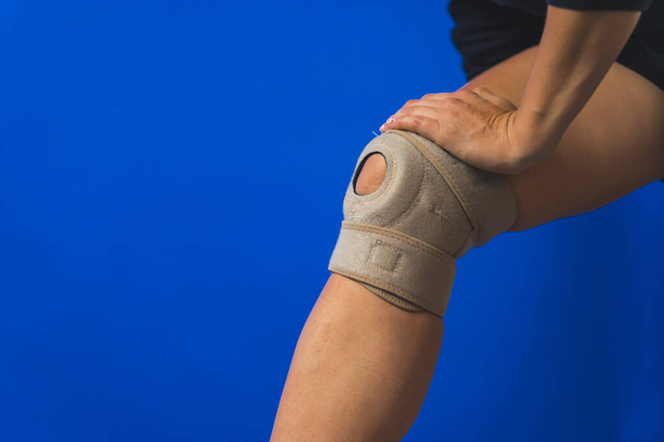 ženy noha s ochranným kolenem rovnátka, modré pozadí zranění a bolesti koncepce. Kvalitní fotografie - Fotografie, Obrázek