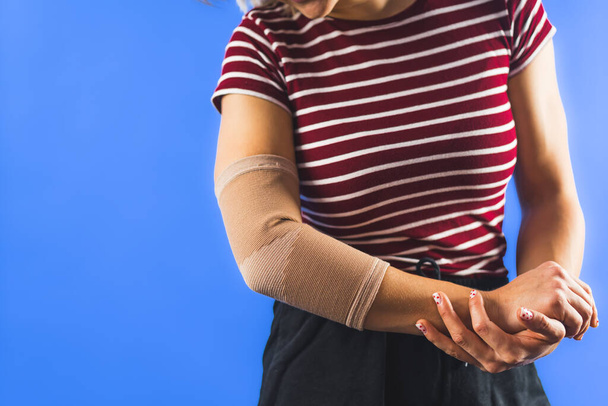 Dirseğinde mavi arka planda bandaj olan genç bir kadın. Yüksek kalite fotoğraf - Fotoğraf, Görsel