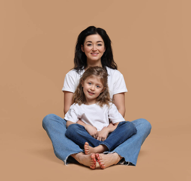 Schöne Mutter mit kleiner Tochter sitzt auf beigem Hintergrund - Foto, Bild