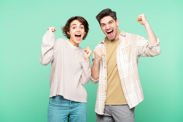 Portrait photo of overjoyed people jumping and shouting, making a "yes" gesture, posing against a turquoise background and looking at the camera - Photo, Image