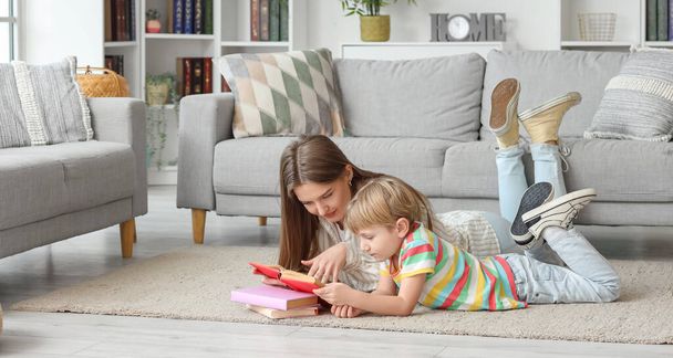 Little boy and his mother reading book while lying on floor at home - Foto, Imagen