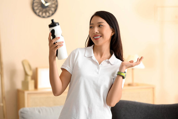 Mooie jonge Aziatische vrouw met fles water thuis. Gewichtsverlies concept - Foto, afbeelding