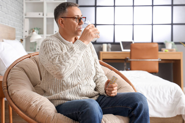 Mężczyzna w średnim wieku ze szklanką wody bierze tabletki w domu - Zdjęcie, obraz