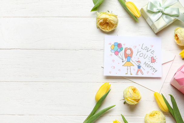 Конверт с детским рисунком, подарочные коробки и цветы на белом деревянном фоне. С Днем матери! - Фото, изображение