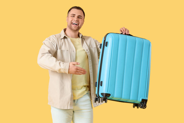 Muž turista ukazující kufr na žlutém pozadí - Fotografie, Obrázek