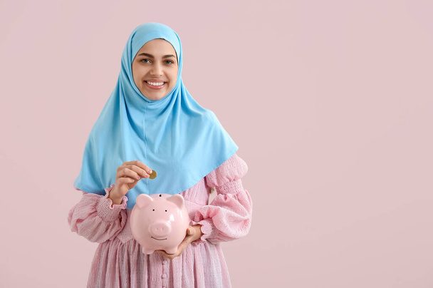 Mulher muçulmana feliz bonita jovem com banco porquinho e moeda no fundo rosa - Foto, Imagem