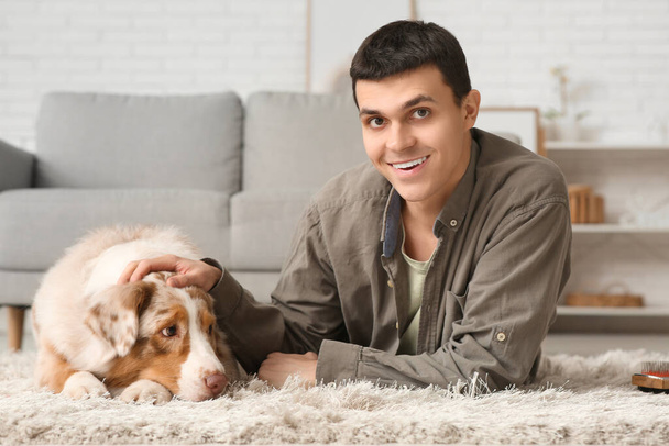 Junger Mann mit australischem Schäferhund liegt zu Hause auf Teppich - Foto, Bild