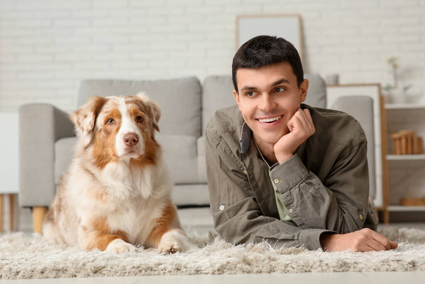 Young man with Australian Shepherd dog lying on carpet at home - Photo, Image