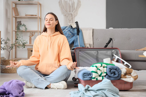 自宅でスーツケースを梱包しながら瞑想する女性観光客 - 写真・画像