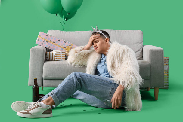 Молодой человек с похмелья рядом с диваном после дня рождения на зеленом фоне - Фото, изображение