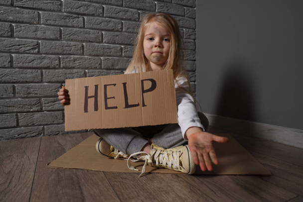 Gri tuğla duvarın yanında yardım dilenen evsiz küçük kız. - Fotoğraf, Görsel