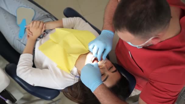 Nuori ruskeaverikkö nainen hammastuolissa. Hammaslääkäri valmistelee potilaan hammashoitoon laittamalla suun suojuksen. Suun ontelon mukava hoito. - Materiaali, video