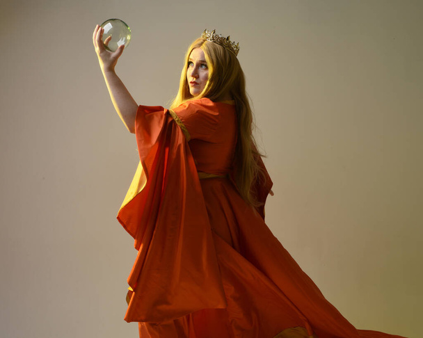 Κοντινό πορτρέτο μιας ξανθιάς γυναίκας, με ιστορικό μεσαιωνικό φόρεμα φαντασίας, χρυσό στέμμα βασιλικής βασίλισσας. gestural χέρια που θέτουν κρατώντας μαγεία κρύσταλλο Seer σφαίρα, απομονωμένο φόντο στούντιο. - Φωτογραφία, εικόνα