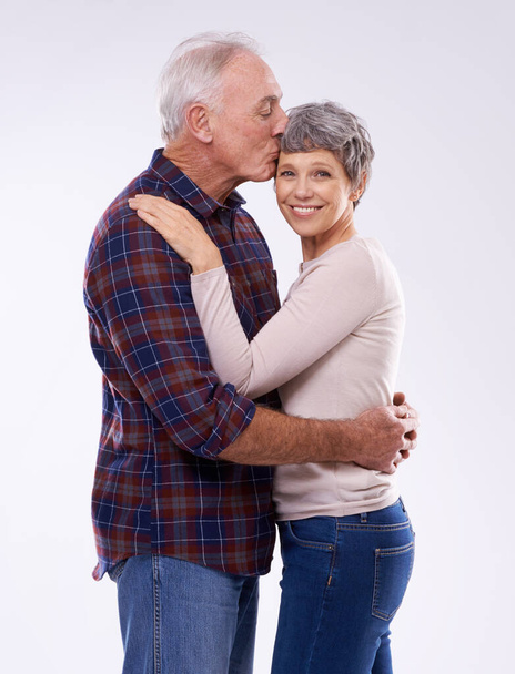 Ritratto, bacio e coppia anziana su sfondo bianco per legame, affetto e relazione felice. Matrimonio, amore e uomini e donne maturi si abbracciano per impegno, fiducia e cura in studio insieme. - Foto, immagini