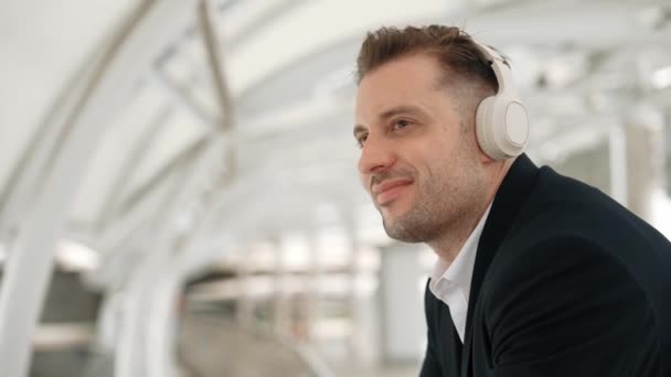 Großaufnahme eines Geschäftsmannes, der seinen Kopf zur Musik bewegt, während er entspannt Lieder aus Kopfhörern hört. Kaukasischer Manager trägt Headset, während er Gesten und Bewegungen in der urbanen Stadt Urbane genießt. - Filmmaterial, Video