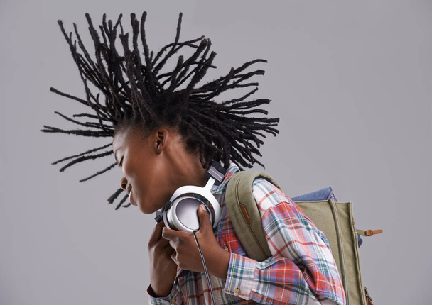 Black child, music and hair flip of a teenager with hip hop and rap audio in a studio. Excited, backpack and student with headphones for radio before school with a happy smile and grey background. - Photo, Image