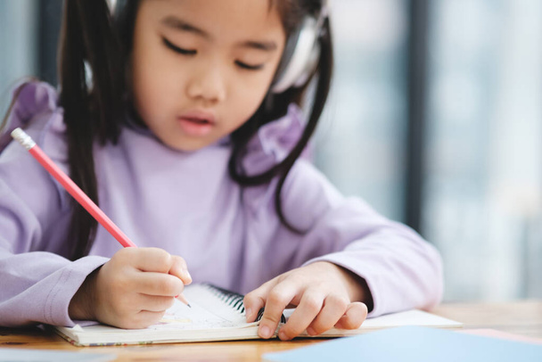 Молодая девушка пишет в блокноте карандашом. На ней наушники и она сосредоточена на работе. Сцена предполагает, что она занята задачей, требующей концентрации - Фото, изображение