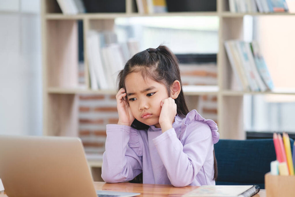 Una joven estudiante parece desinteresada y aburrida mientras participa en una clase en línea en su computadora portátil. - Foto, imagen