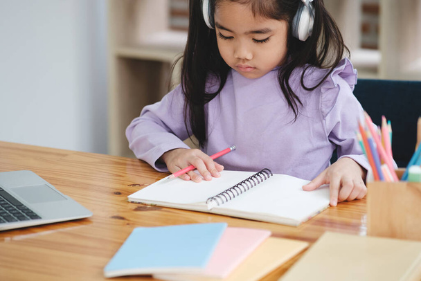 Una giovane ragazza è seduta a una scrivania con un notebook e un computer portatile. Indossa le cuffie ed è concentrata sul suo lavoro - Foto, immagini