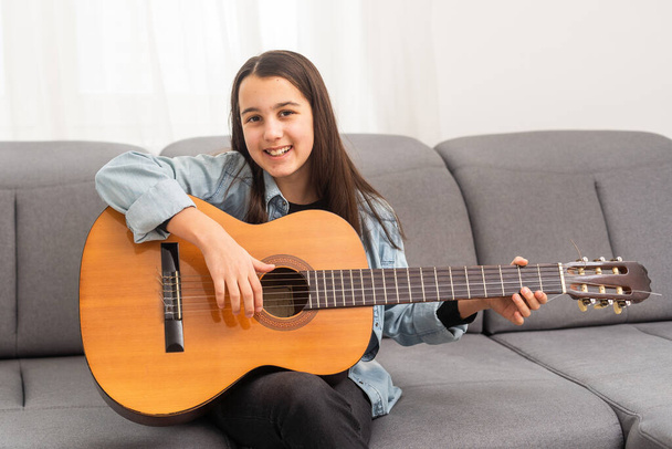 Портрет улыбающегося подростка, практикующего гитару во время уроков музыки. Высокое качество фото - Фото, изображение