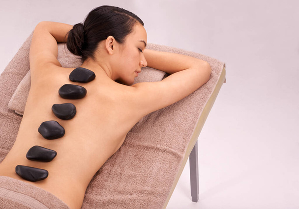 Spa, woman and massage with hot stone therapy and wellness with vacation and stress relief. Natural, person and girl with peace or calm with holiday and weekend break with skin detox or luxury resort. - Photo, Image