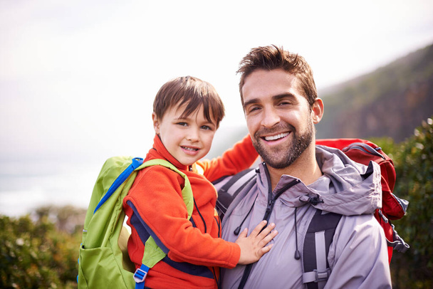 Dad, child and portrait with hiking, backpack and travel with smile and support in nature. Kid, adventure and mountain with love, trust and bonding together with family and journey for holiday. - Photo, Image