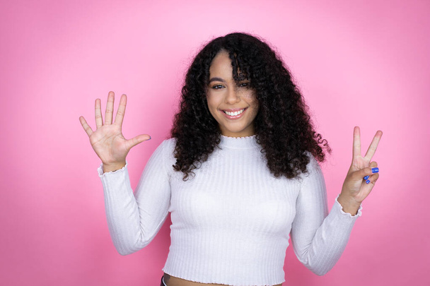 Femme afro-américaine portant un pull décontracté sur fond rose montrant et pointant vers le haut avec les doigts numéro sept tout en souriant confiant et heureux - Photo, image