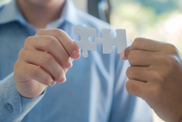 Two people holding a puzzle piece together. Concept of teamwork and collaboration. Scene is positive and uplifting, as it shows two people working together to solve a problem - Photo, Image