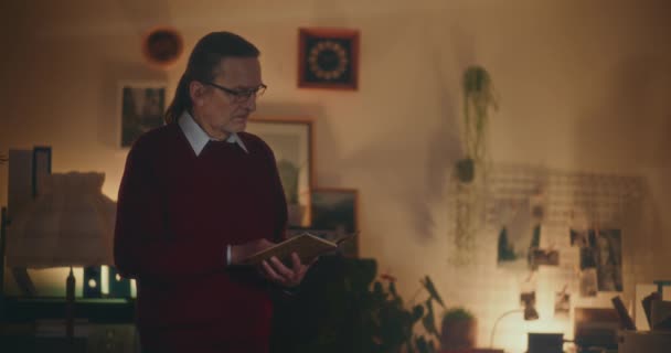Homme âgé plongé dans la lecture nocturne, captivé par un livre sous une lumière douce et tamisée dans le confort de la maison - Séquence, vidéo