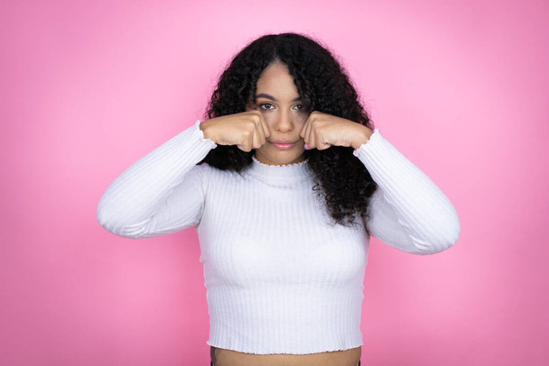 Αφροαμερικανή γυναίκα που φοράει casual πουλόβερ πάνω από ροζ φόντο κατάθλιψη και ανησυχούν για την αγωνία, κλάμα θυμωμένος και φοβισμένος. Θλιβερή έκφραση. - Φωτογραφία, εικόνα