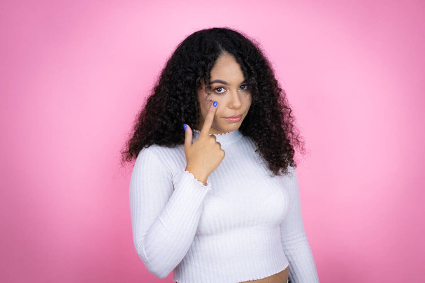African american woman wearing casual sweater over pink background Pointing to the eye watching you gesture, suspicious expression - Photo, Image