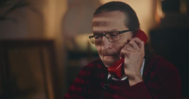 Elderly gentleman engages in nostalgic conversation on a vintage telephone under the quiet ambiance of night - Footage, Video