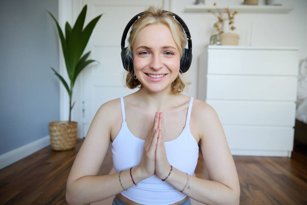 Welzijn en mensen concept. close-up portret van jonge vrouw in hoofdtelefoon, mediteren, praktijk yoga, luistert naar podcast in oortelefoons. - Foto, afbeelding