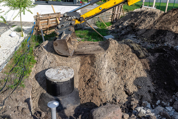 Usando una excavadora para enterrar un tanque séptico de hormigón de 10 m3 ubicado en el jardín junto a la casa. - Foto, Imagen