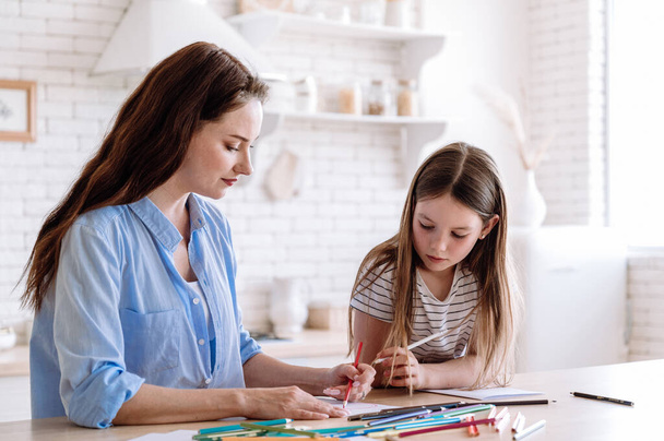 Çocukların yaratıcılık konsepti. Küçük çocuklu renkli kalemlerle kağıda resim çizen genç bir anne ya da dadı. Anne ve kızı hafta sonunu rahat bir evde geçiriyorlar. - Fotoğraf, Görsel