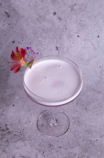 Image élégante d'un cocktail rose dans un verre avec une garniture de fleurs sur un fond gris, exsudant classe et sophistication. - Photo, image