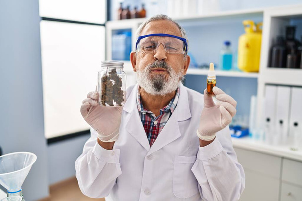 Zabawny wyraz twarzy seniora nadymiającego policzki trzymającego medyczną marihuanę w laboratorium, usta napompowane powietrzem dla śmiesznej twarzy, wywołującej radosne wibracje rozruchów śmiechu - Zdjęcie, obraz