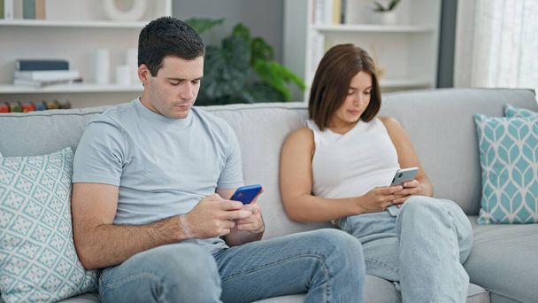 Gyönyörű pár ül a kanapén együtt használja okostelefonok otthon - Fotó, kép