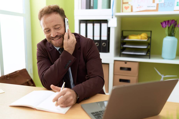 Középkorú férfi üzletember beszél okostelefon írás notebook az irodában - Fotó, kép