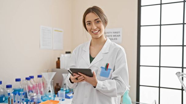 Donna scienziata sorridente con tablet in laboratorio circondata da attrezzature e becher - Foto, immagini