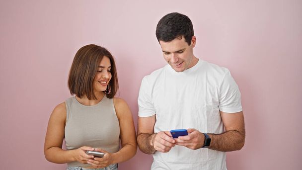 Beau couple souriant confiant en utilisant des smartphones sur fond rose isolé - Photo, image
