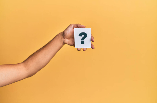 Hand of caucasian man holding paper with question mark over isolated yellow background - Foto, immagini