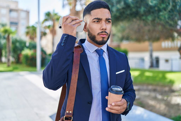 若いラテン人ビジネスワーカーが公園でコーヒーを飲むスマートフォンで音声メッセージを聞く - 写真・画像